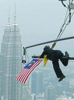 Afbeelding: Stunt director van het Zuid-Afikaanse produktiehuis Francois Grobelaan vervangt een Fear Factor vlag met de Jalur Gemilang, de nationale vlag van Maleisië, op de KL Tower."