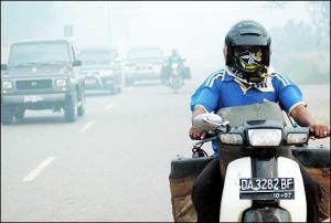 Afbeelding: Een motorrijder op Borneo trotseert de rook."